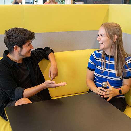 Twee collega’s praten glimlachend met elkaar bij TOPdesk op kantoor in Delft.