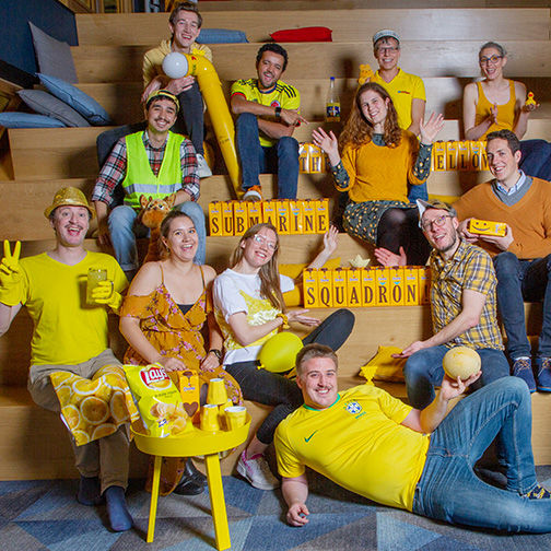 Team Yellow Submarine Squadron poseert in gele outfits in het auditorium op kantoor bij TOPdesk in Delft. 