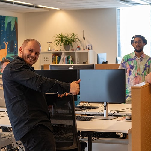 Twee collega’s staan bij hun bureau op het TOPdesk hoofdkantoor in Delft.